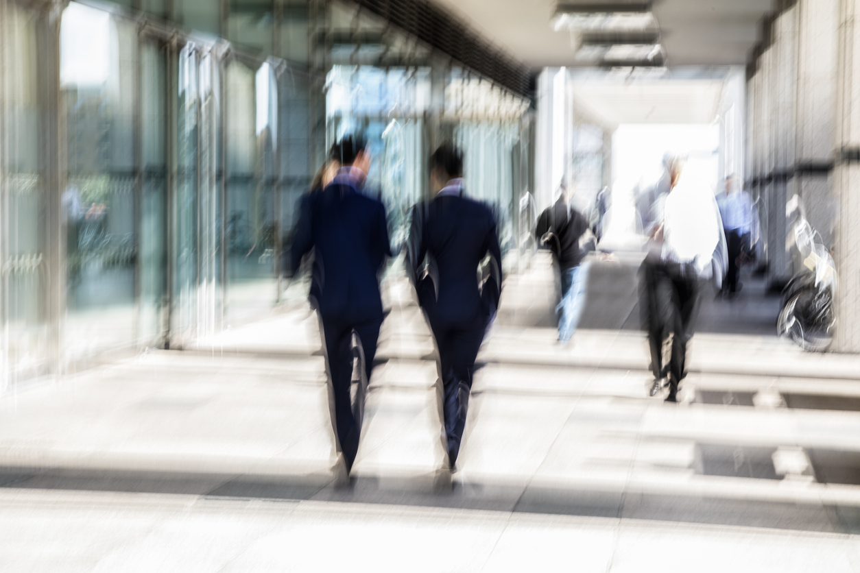 Two men in suits walking together along a city sidewalk, captured with motion blur