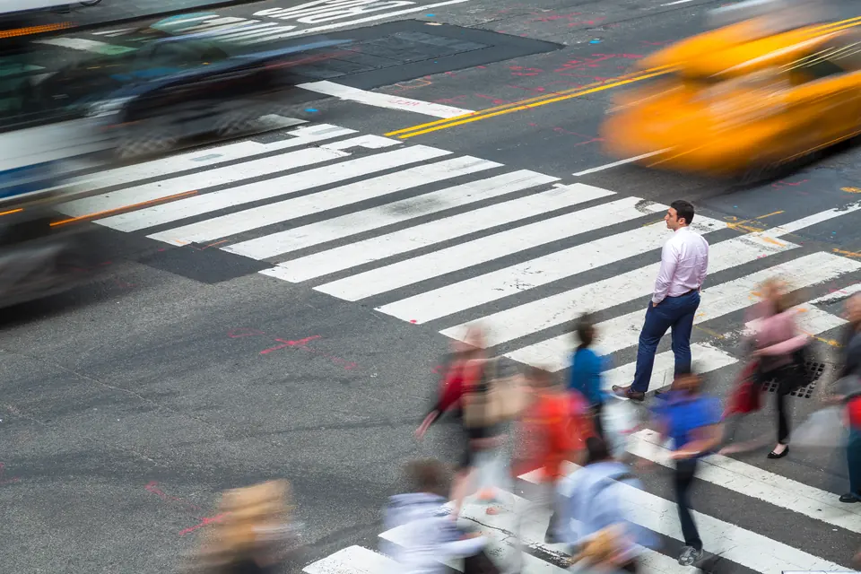 A man standing at a city crossing while traffic and people pass