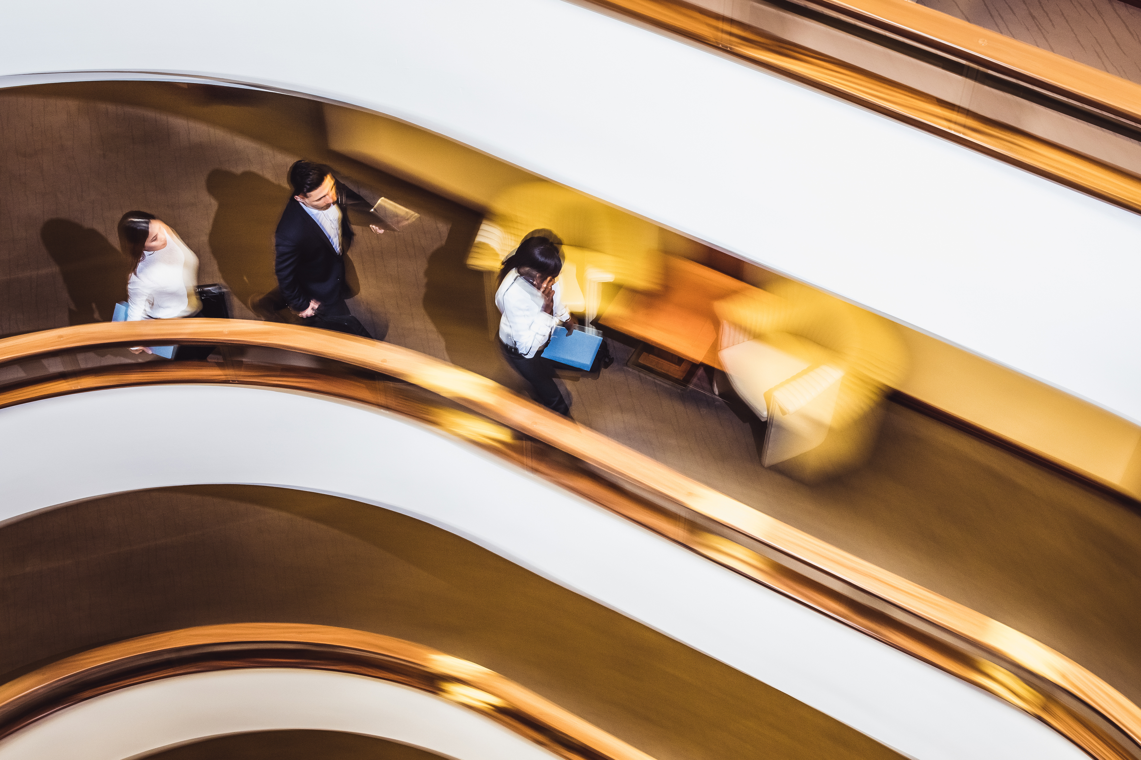 An overhead view of people walking along a curved office corridor with golden railings and motion blur
